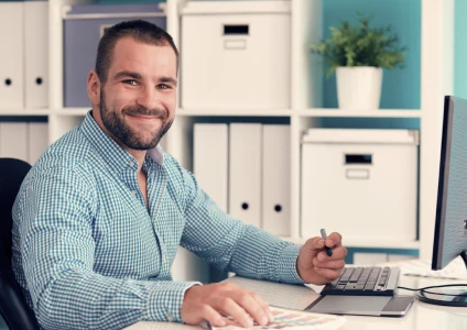 Homem empresário sorrindo para foto enquanto faz anotações em computador